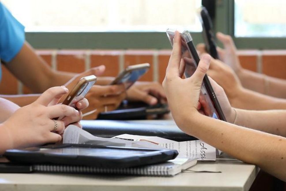 Schüler und Schülerinnen arbeiten mit Tablets und Smartphones an einem Schreibtisch.