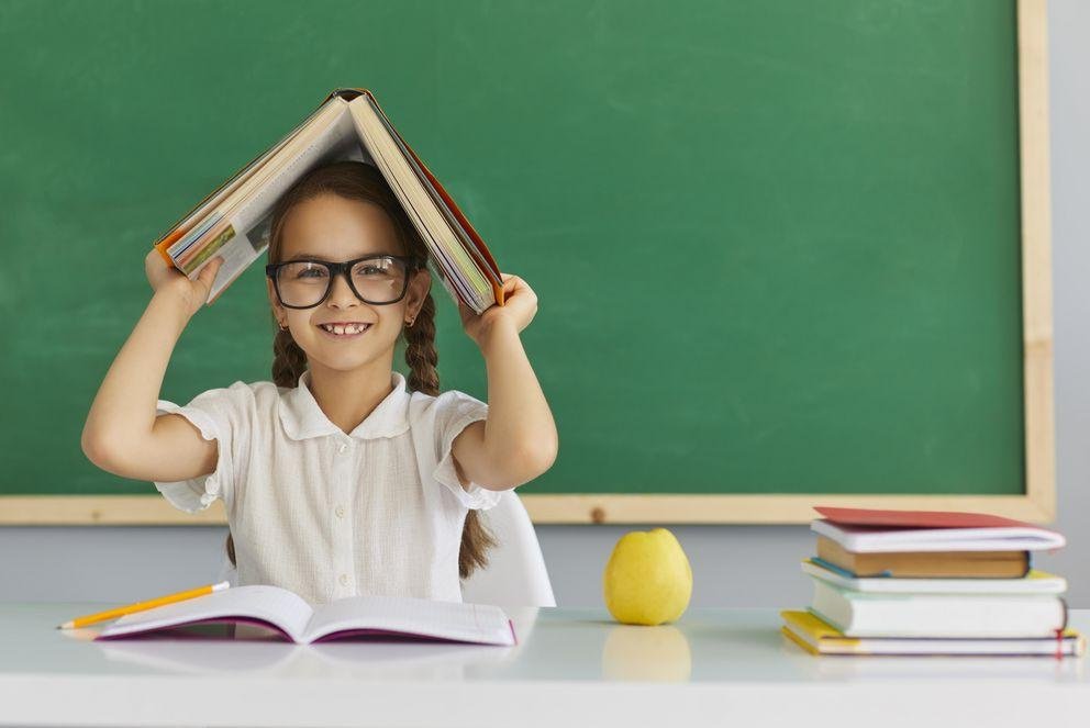 Schulmädchen mit einem Buch über dem Kopf