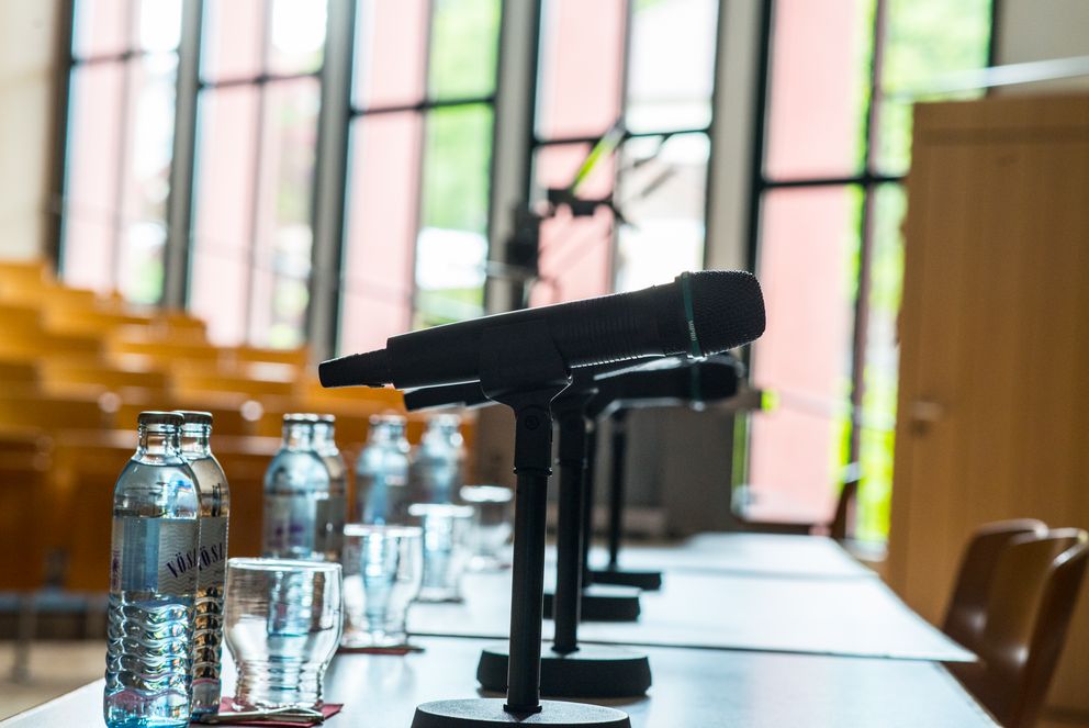Mikrofone und Wasserflaschen stehen auf Tischen im Audimax, die für die Diskussionsteilnehmer bereitgestellt wurden.