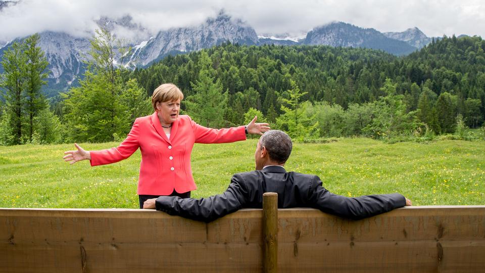 "Merkel-Meme": Angela Merkel und Barack Obama vor idyllischer Alpenkulisse 2015 auf dem G7-Gipfel. Die Kanzlerin breitet die Arme aus, der ehemalige US-Präsident sitzt mit dem Rücken zum Publikum lässig auf einer Bank. Foto: Pete Souza, Official White House Photo